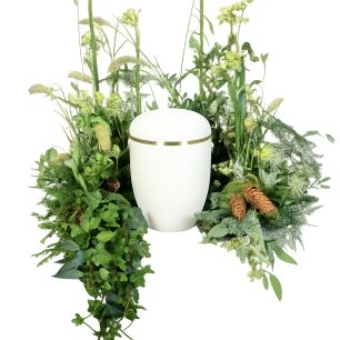 Vit urna omgiven av grönska och blommor, med dekorativa kottar.