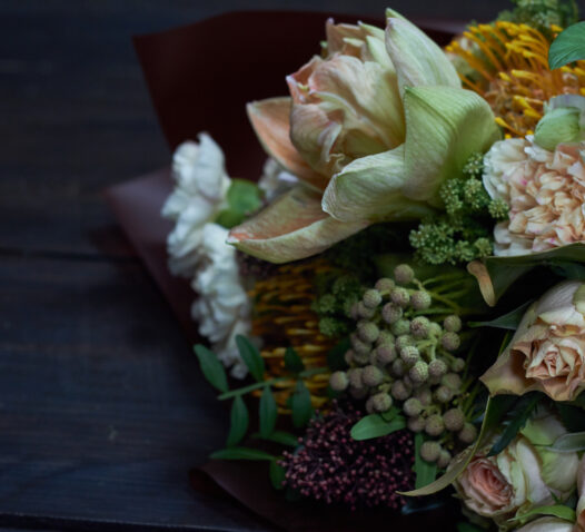 En närbild av en bukett med olika blommor och gröna blad mot en mörk bakgrund.