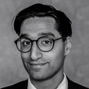 A person with short dark hair and glasses, smiling slightly in a grayscale portrait.